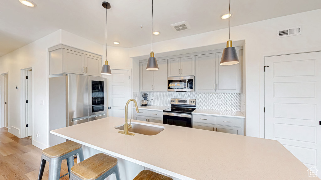 Kitchen with appliances with stainless steel finishes, a sink, tasteful backsplash, a breakfast bar area, and light wood-style floors