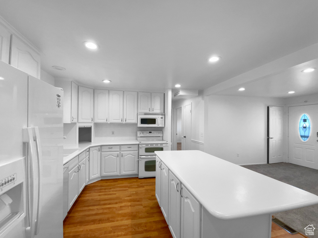 Kitchen featuring white appliances, recessed lighting, a center island, white cabinets, and light countertops
