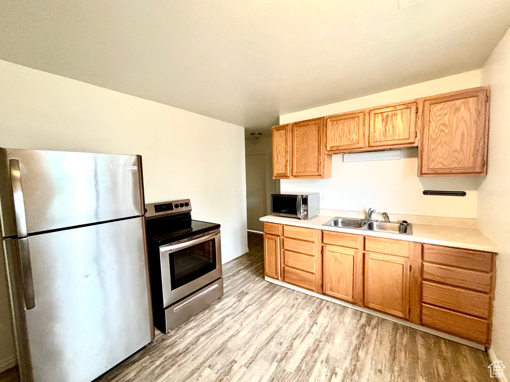 Kitchen with stainless steel appliances, light wood finished floors, a sink, and light countertops
