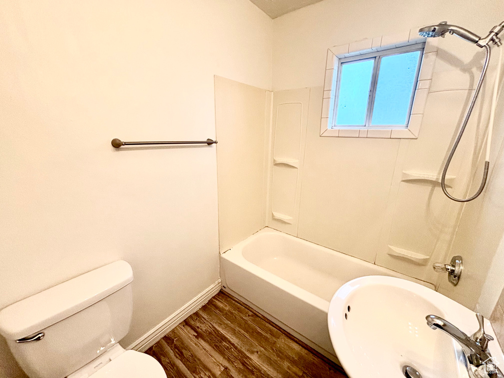 Full bath with wood finished floors, a sink, toilet, baseboards, and washtub / shower combination