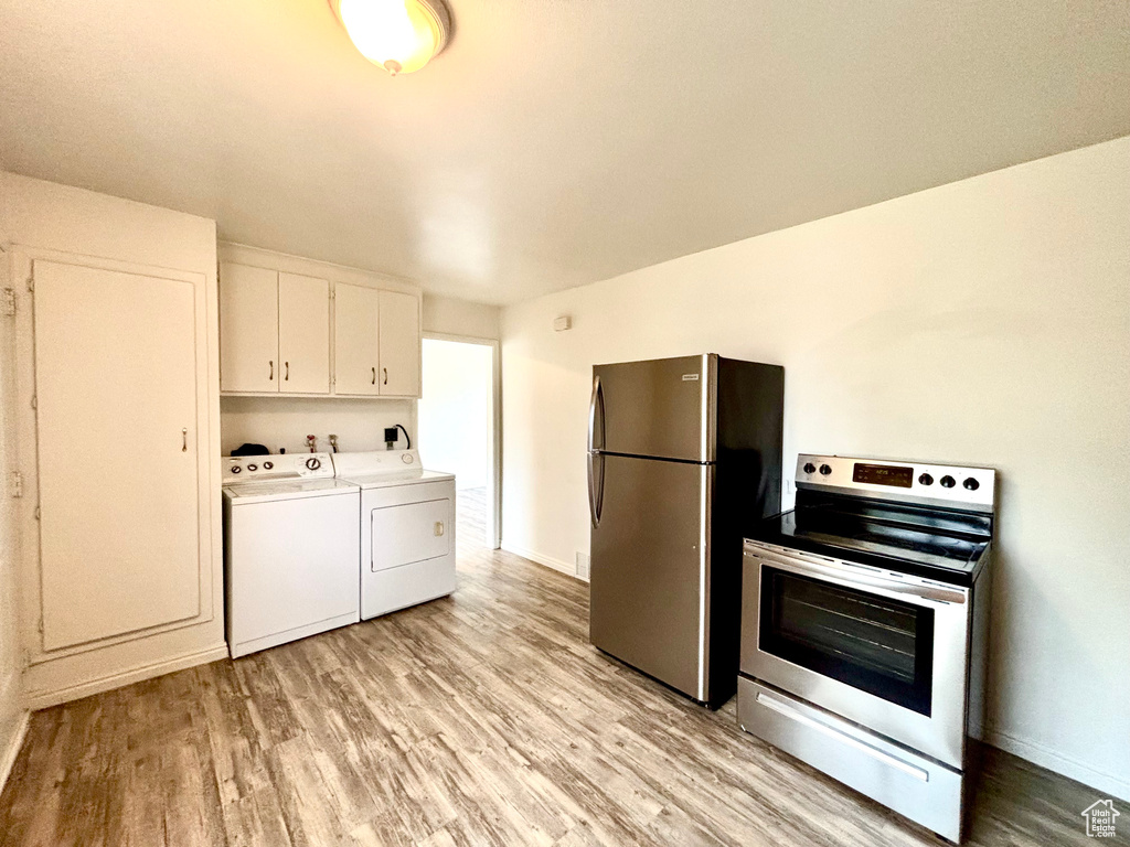 Kitchen featuring appliances with stainless steel finishes, washing machine and dryer, light wood-style floors, light countertops, and white cabinetry