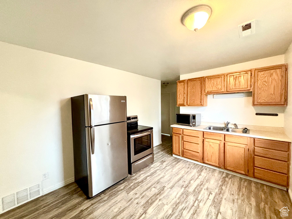 Kitchen featuring appliances with stainless steel finishes, light wood-style floors, light countertops, a sink, and baseboards