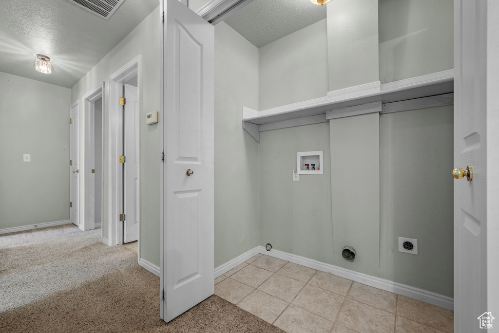 Clothes washing area with electric dryer hookup, hookup for a washing machine, a textured ceiling, tile patterned floors, and baseboards