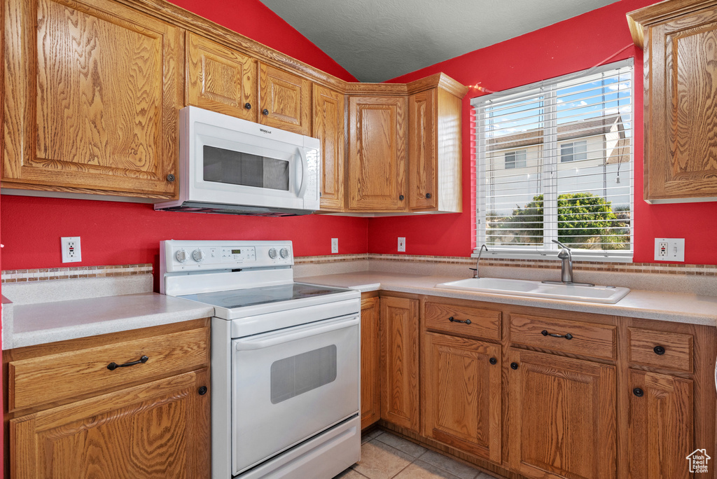 Kitchen featuring white appliances, a sink, vaulted ceiling, light countertops, and light tile patterned flooring