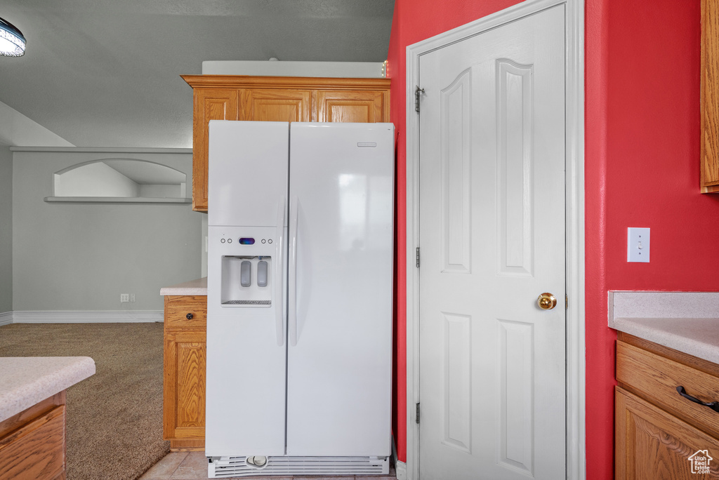 Kitchen featuring white refrigerator with ice dispenser, light colored carpet, light countertops, and baseboards