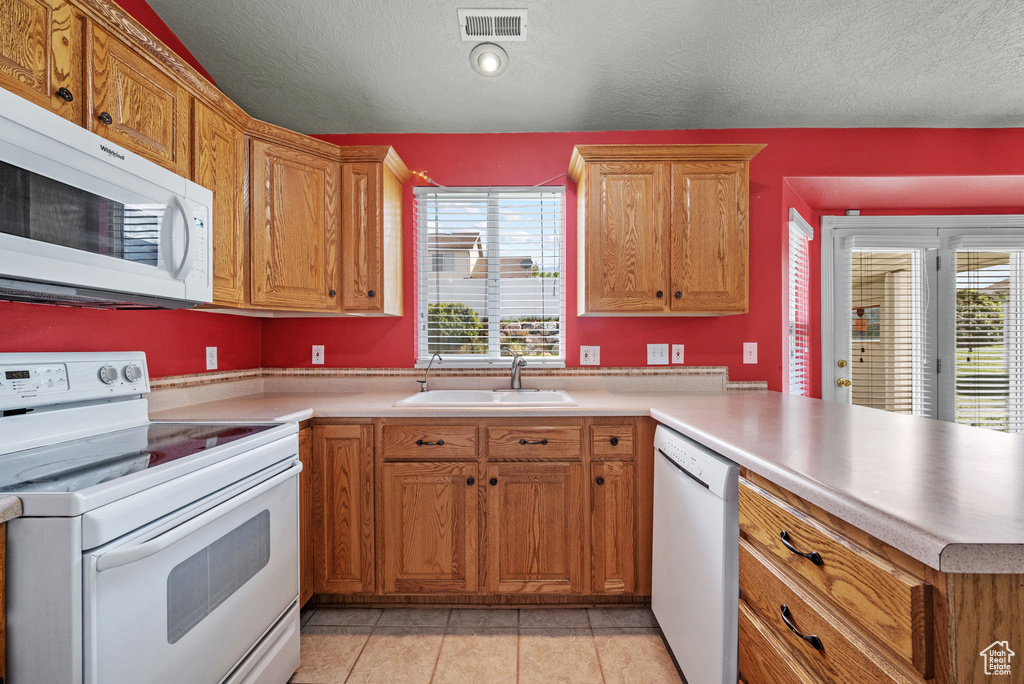 Kitchen featuring white appliances, a sink, a peninsula, light countertops, and light tile patterned floors