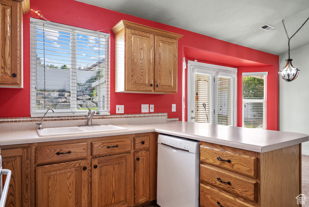 Kitchen with dishwasher, a sink, a peninsula, light countertops, and hanging light fixtures