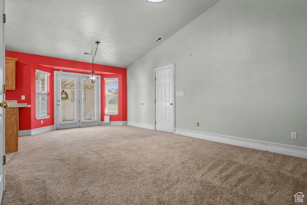 Carpeted empty room with vaulted ceiling, baseboards, and a textured ceiling
