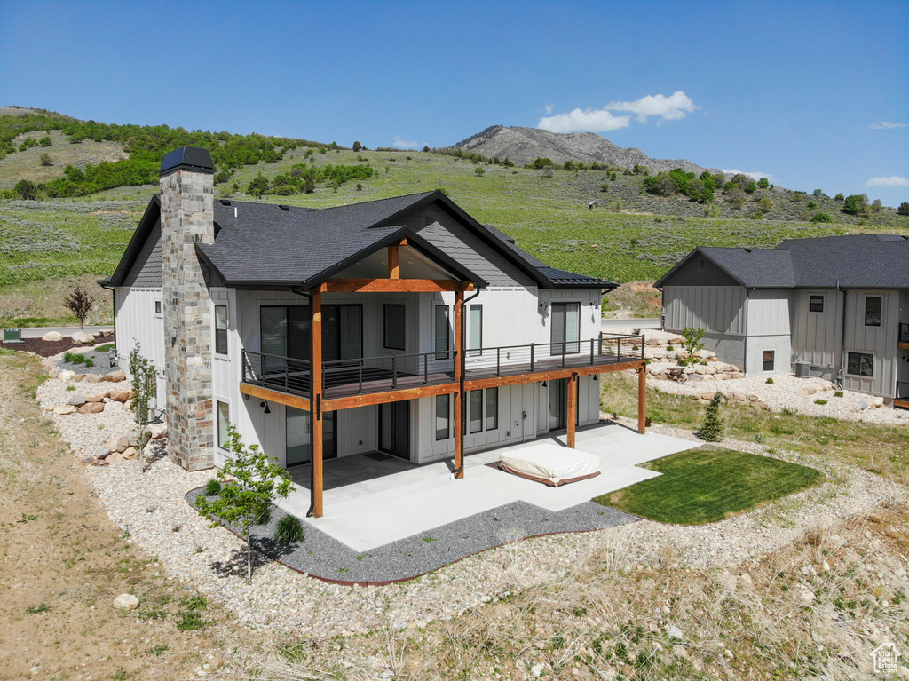 Back of property with a patio, board and batten siding, a deck with mountain view, a chimney, and a shingled roof