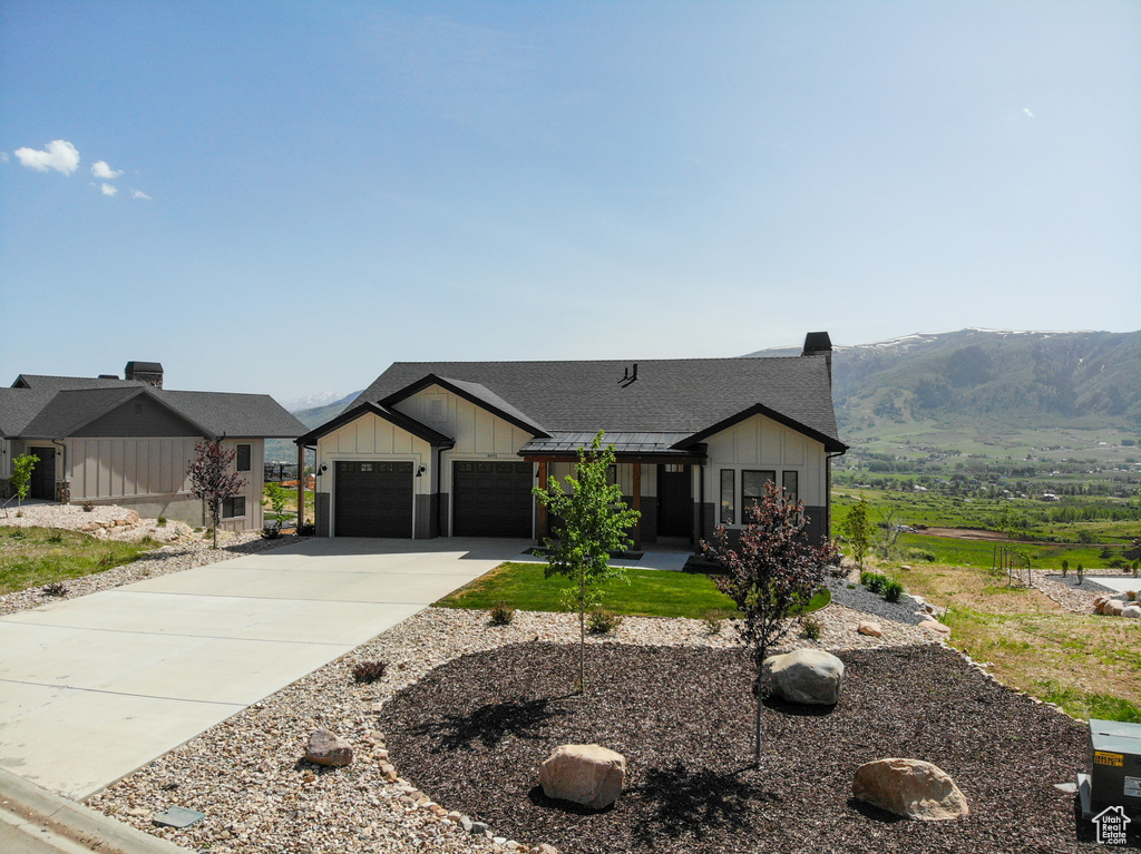 Modern farmhouse with board and batten siding, concrete driveway, a shingled roof, a garage, and a mountain view