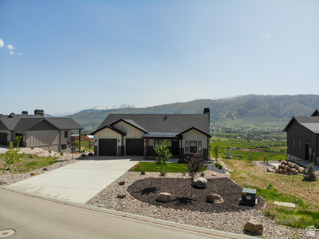 Modern farmhouse style home with a mountain view, concrete driveway, an attached garage, board and batten siding, and a chimney