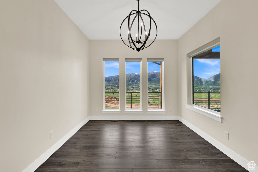 Unfurnished dining area featuring a chandelier, baseboards, dark wood finished floors, and a mountain view