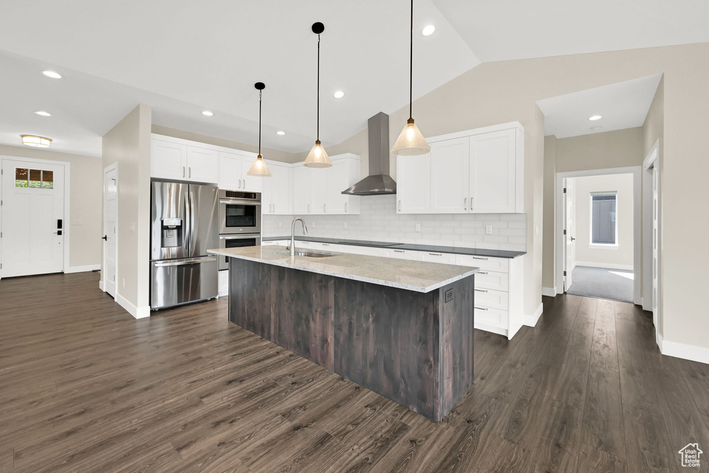 Kitchen featuring stainless steel appliances, wall chimney range hood, a sink, decorative backsplash, and dark wood finished floors
