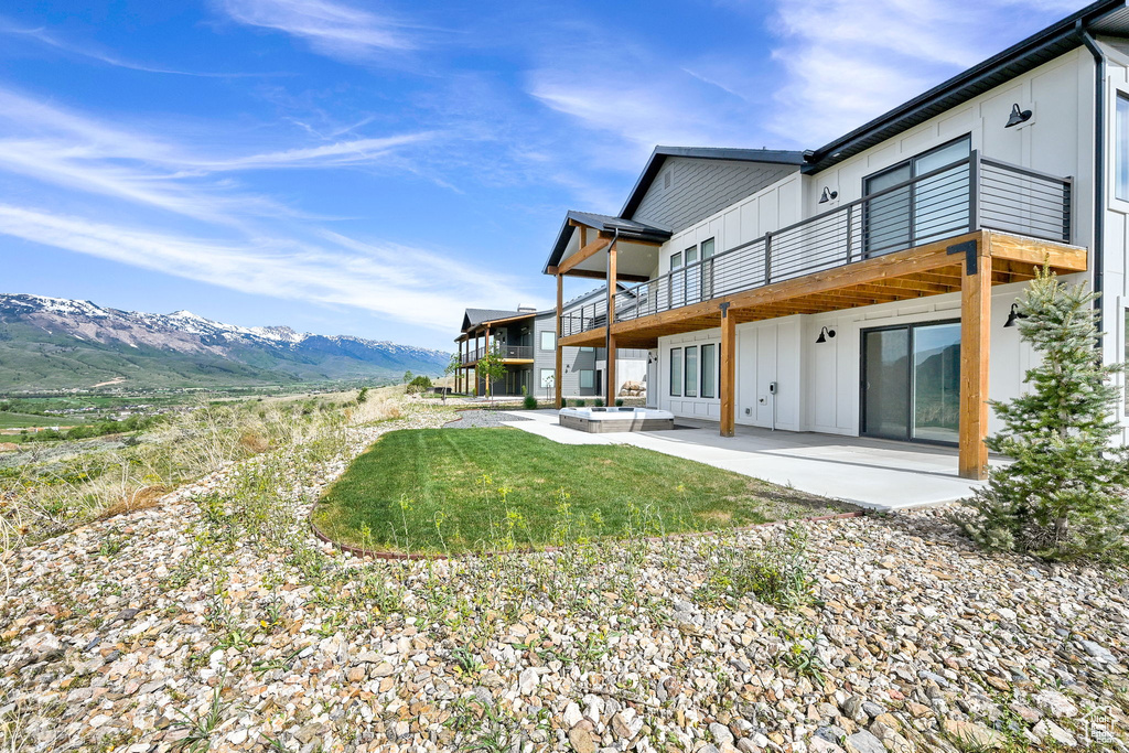 Back of property featuring board and batten siding, a patio, a balcony, a mountain view, and outdoor lounge area