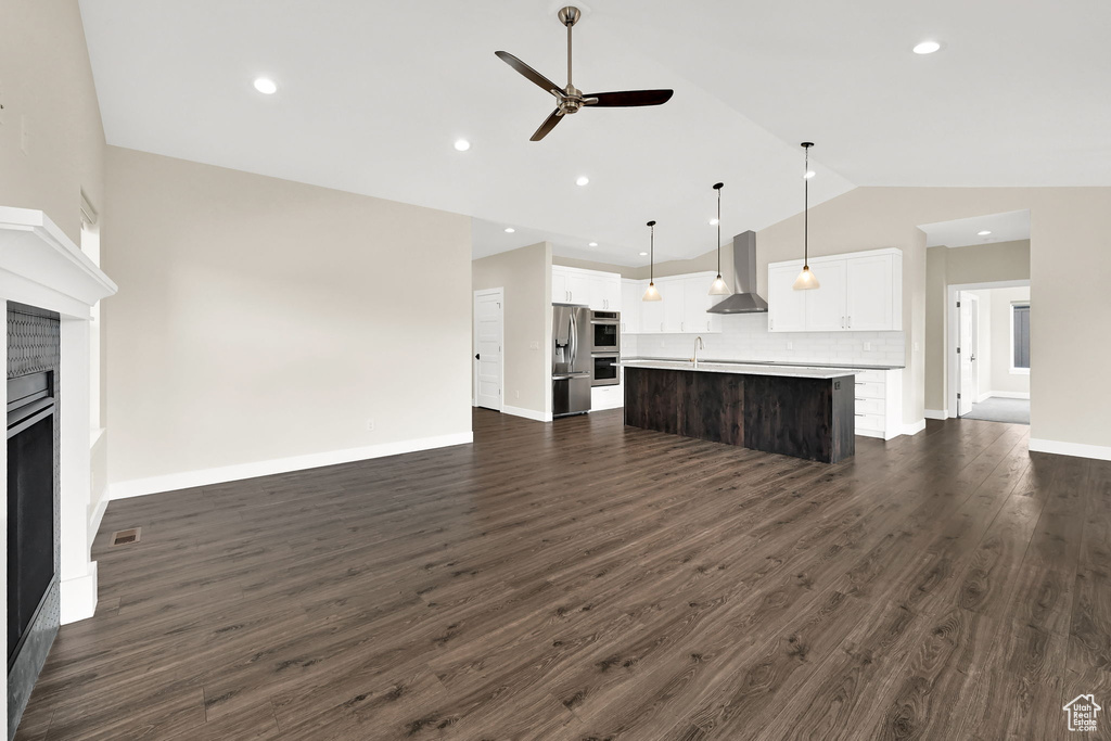 Unfurnished living room featuring vaulted ceiling, ceiling fan, a fireplace, dark wood finished floors, and baseboards