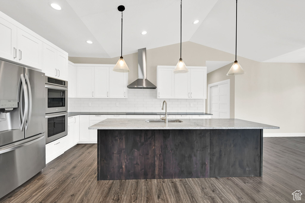 Kitchen with appliances with stainless steel finishes, wall chimney exhaust hood, a sink, dark wood finished floors, and decorative backsplash