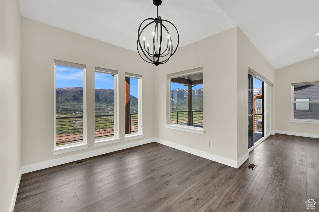 Unfurnished dining area with dark wood-type flooring, a chandelier, vaulted ceiling, baseboards, and a mountain view