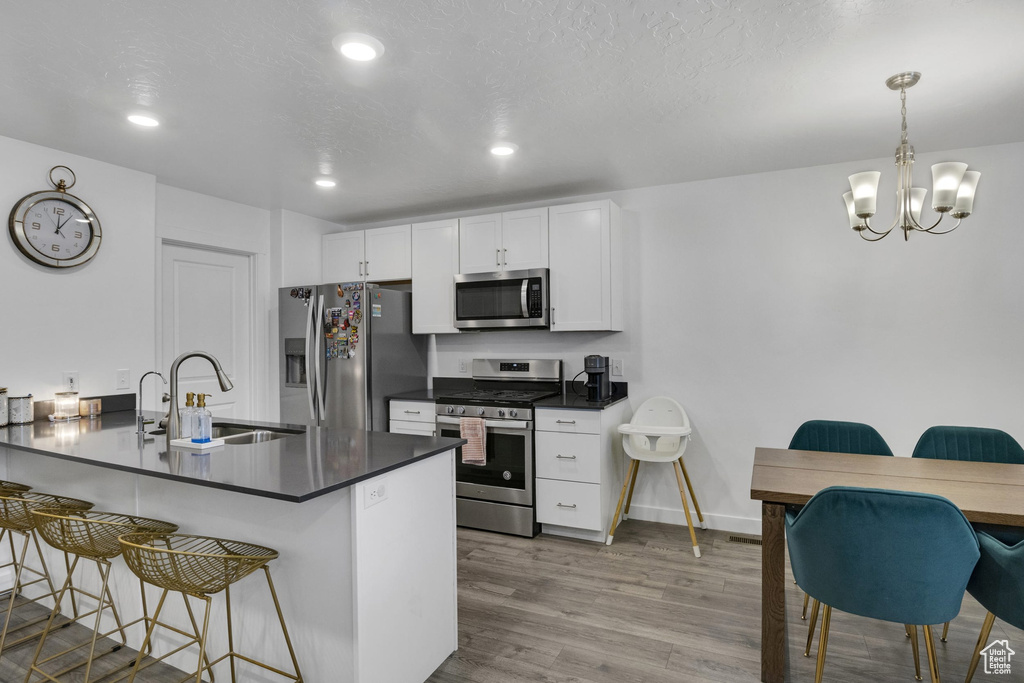 Kitchen featuring stainless steel appliances, a sink, a breakfast bar area, dark countertops, and white cabinets