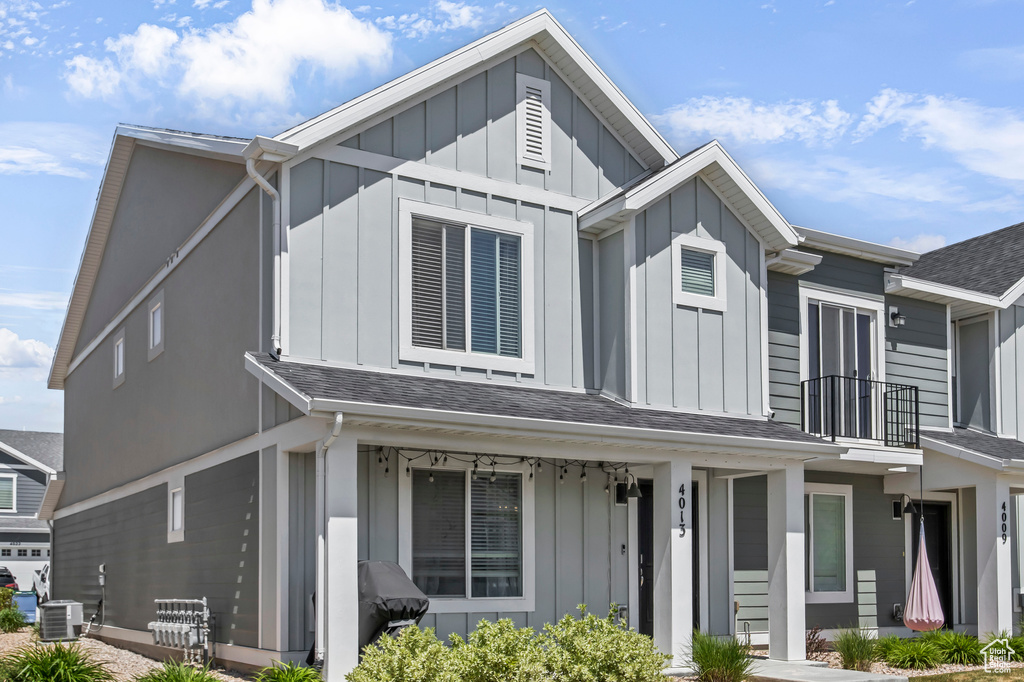 View of front of property with board and batten siding, cooling unit, a balcony, and a shingled roof