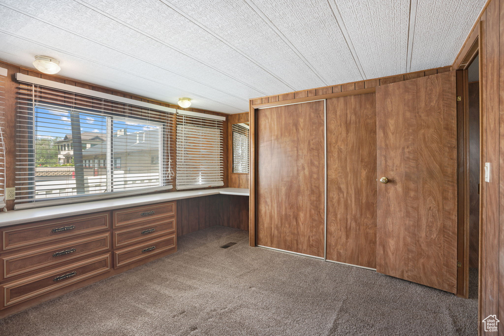 Unfurnished bedroom with carpet flooring, wooden walls, and a closet