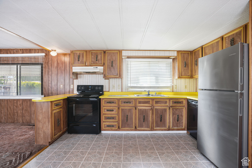 Kitchen featuring black appliances, under cabinet range hood, a sink, brown cabinets, and wooden walls