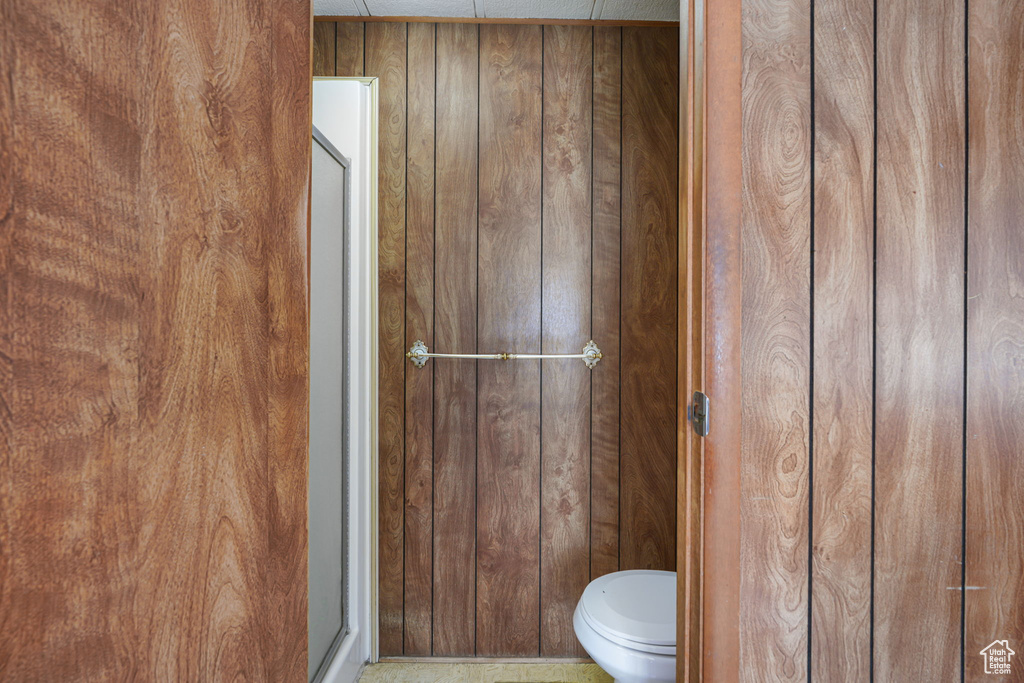 Bathroom with wood walls, toilet, and a shower with shower door
