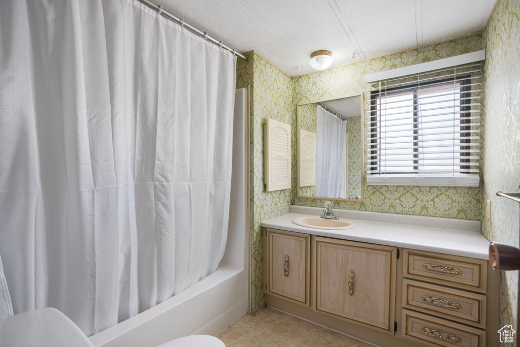 Full bathroom featuring wallpapered walls, vanity, and shower / tub combo with curtain