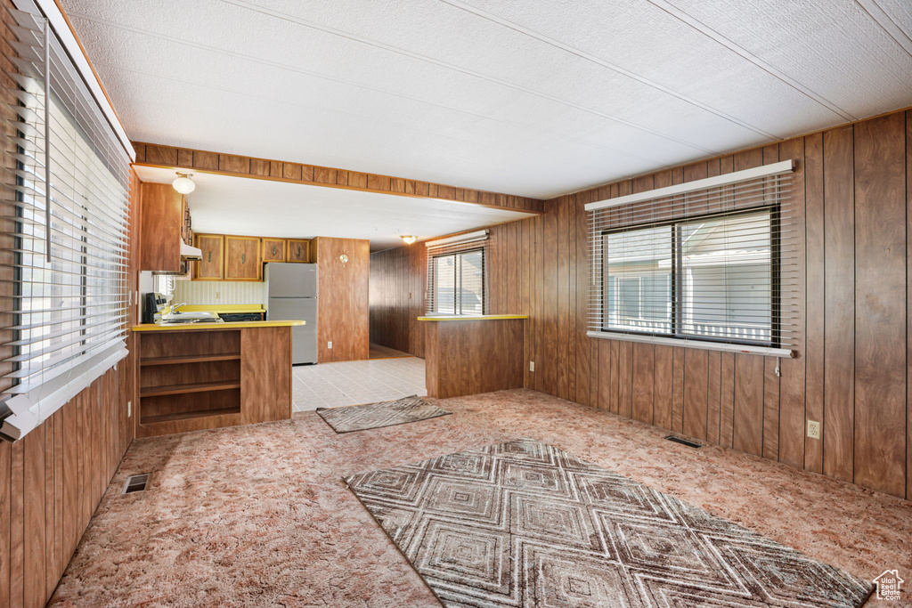 Kitchen featuring freestanding refrigerator, wood walls, light carpet, brown cabinetry, and light countertops