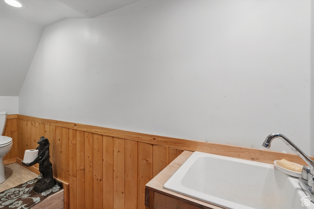 Bathroom with a sink, toilet, wainscoting, vaulted ceiling, and wood walls
