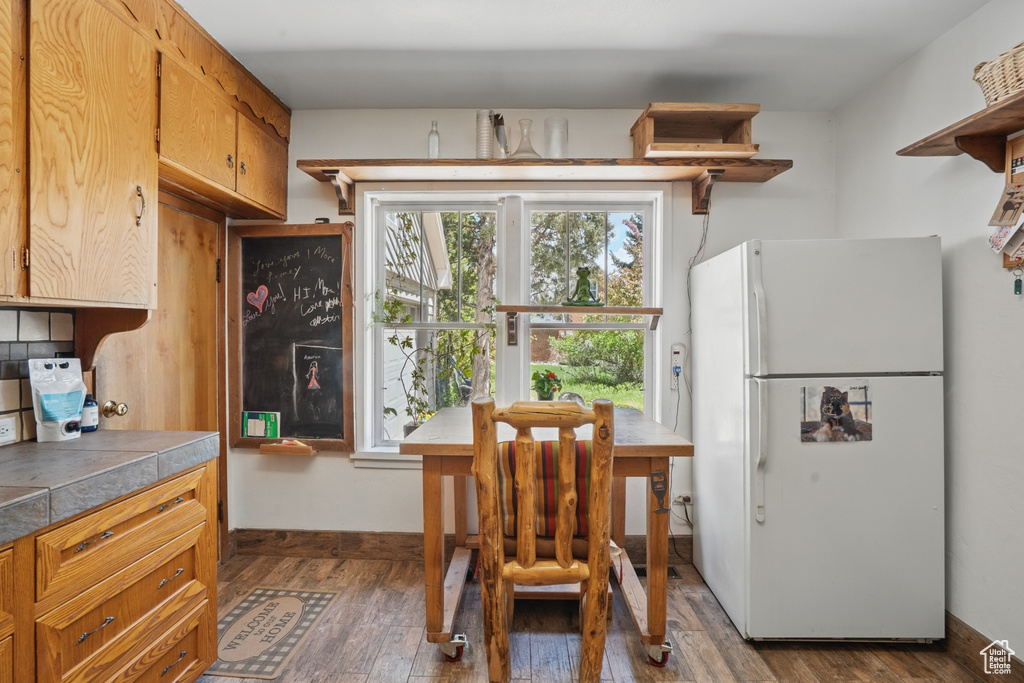 Kitchen featuring freestanding refrigerator, open shelves, dark wood-style floors, and tile countertops