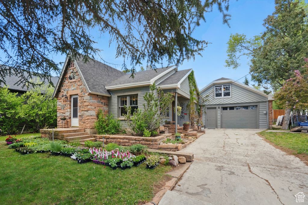 View of front of house featuring stone siding, a front yard, a shingled roof, and a garage