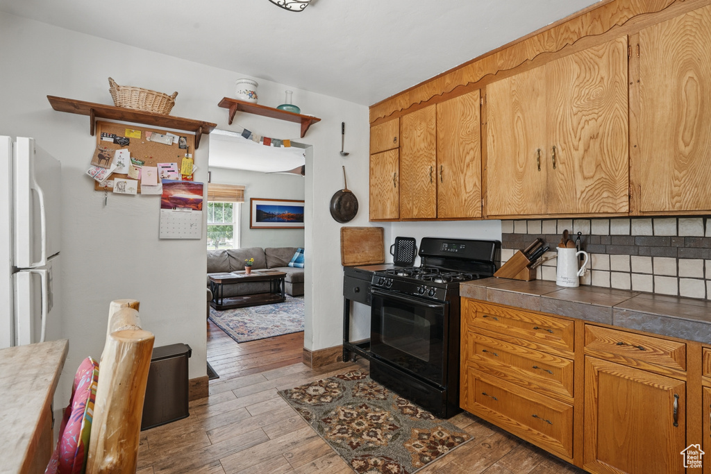 Kitchen with black range with gas stovetop, freestanding refrigerator, hardwood / wood-style flooring, tasteful backsplash, and dark countertops