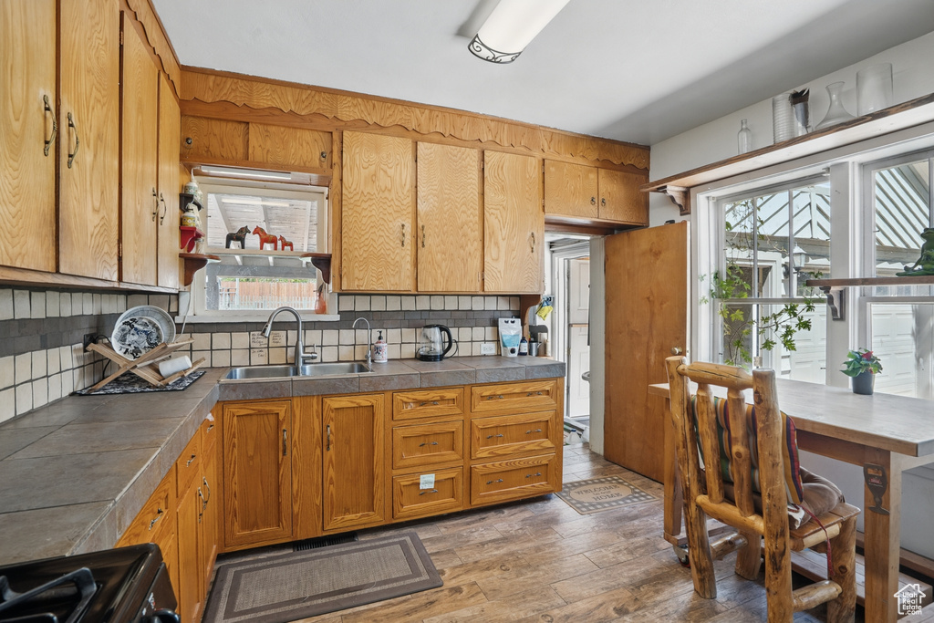 Kitchen featuring a sink, light wood-style flooring, black gas range, backsplash, and plenty of natural light