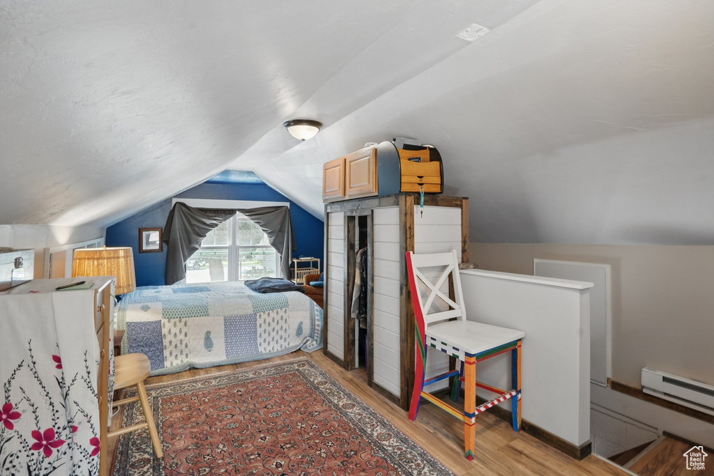 Bedroom with wood finished floors, lofted ceiling, and a baseboard heating unit