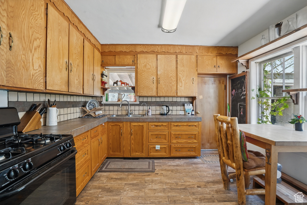 Kitchen with black gas range oven, a sink, backsplash, light wood-style floors, and brown cabinetry