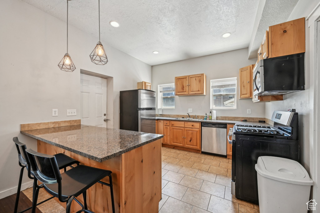 Kitchen featuring stainless steel appliances, a peninsula, a sink, a textured ceiling, and a kitchen bar