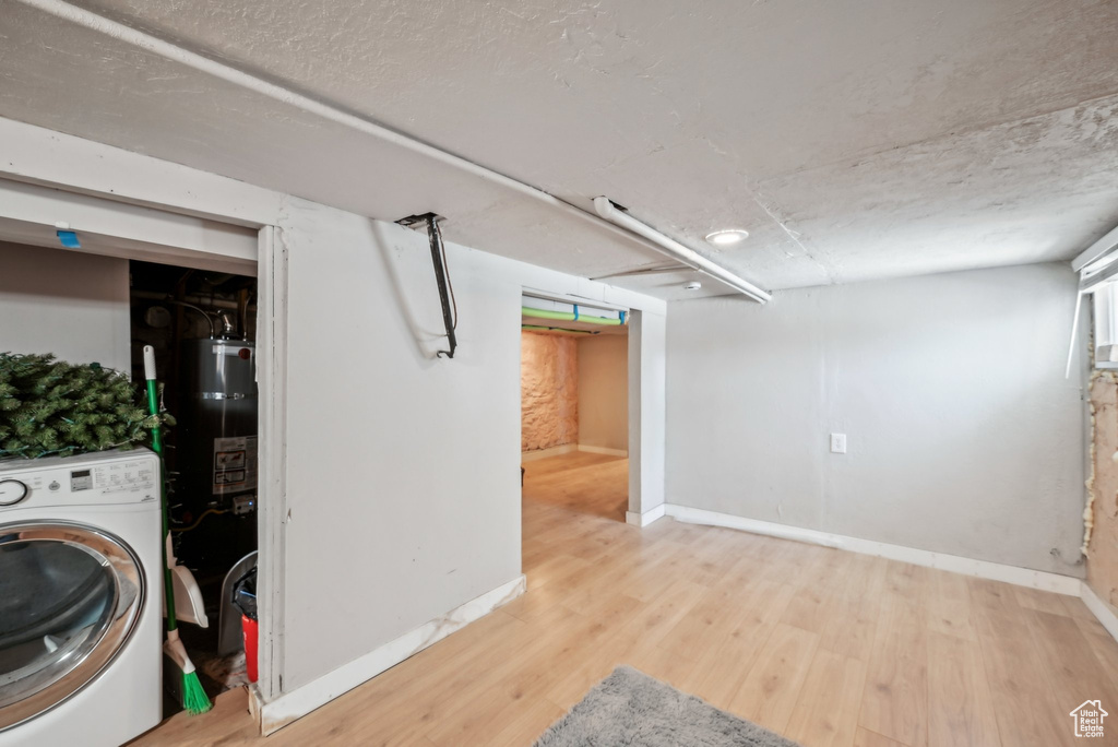 Finished below grade area featuring washer / dryer, wood finished floors, strapped water heater, and baseboards