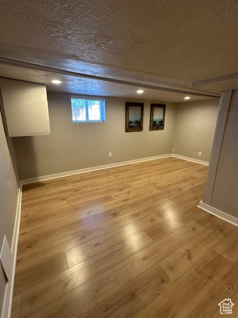Basement with light wood finished floors, a textured ceiling, and baseboards