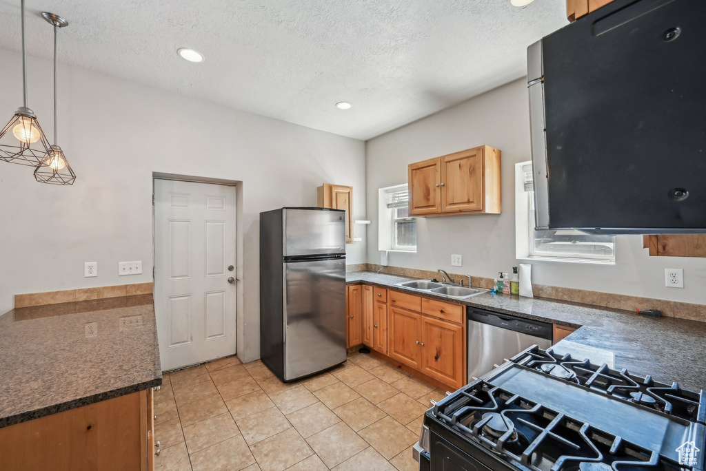 Kitchen with stainless steel appliances, a sink, dark countertops, decorative light fixtures, and a textured ceiling