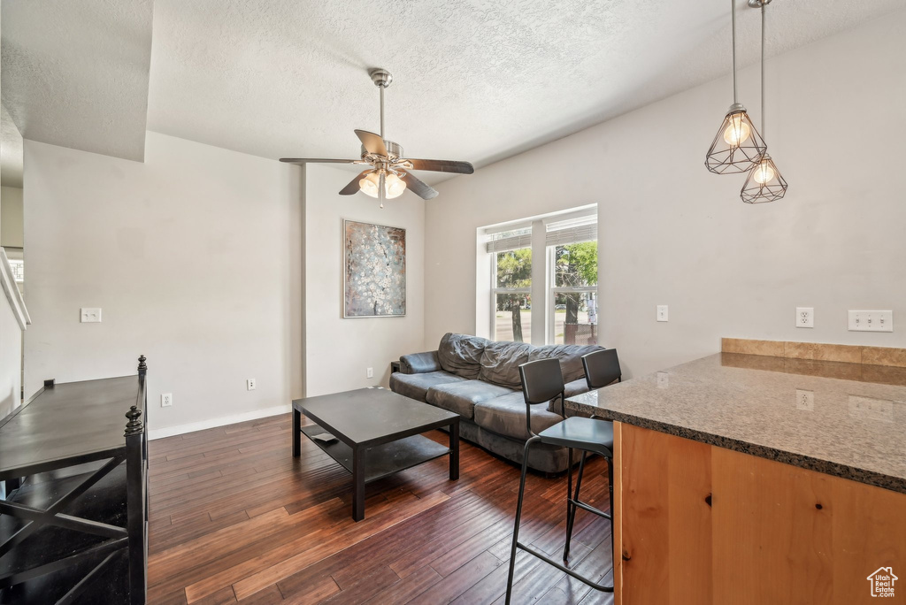 Living area featuring a ceiling fan, dark wood-style floors, a textured ceiling, and baseboards