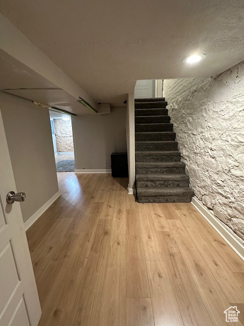 Finished below grade area with stairs, light wood-type flooring, baseboards, and recessed lighting