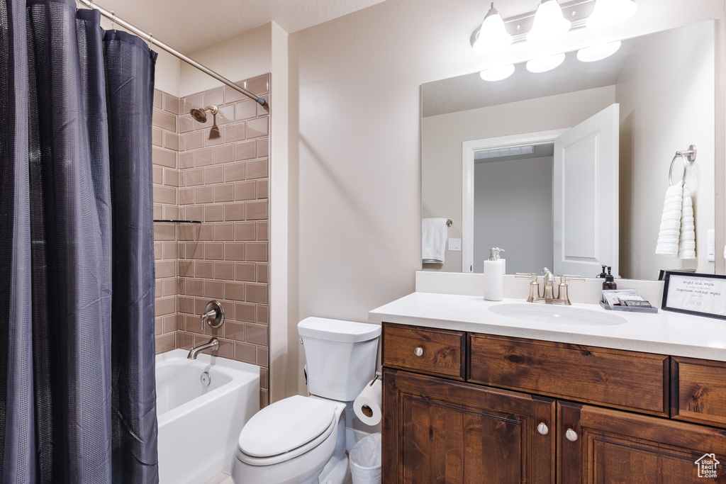 Bathroom featuring toilet, shower / bathtub combination with curtain, and vanity