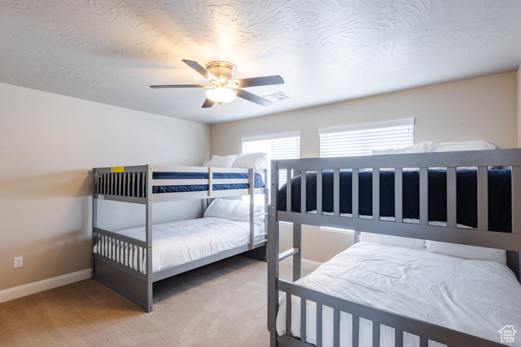 Carpeted bedroom with multiple windows, ceiling fan, and baseboards