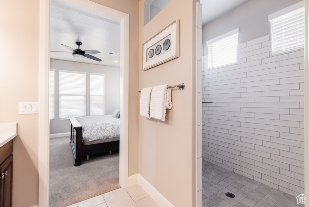 Ensuite bathroom featuring ceiling fan, vanity, tiled shower, tile patterned flooring, and baseboards