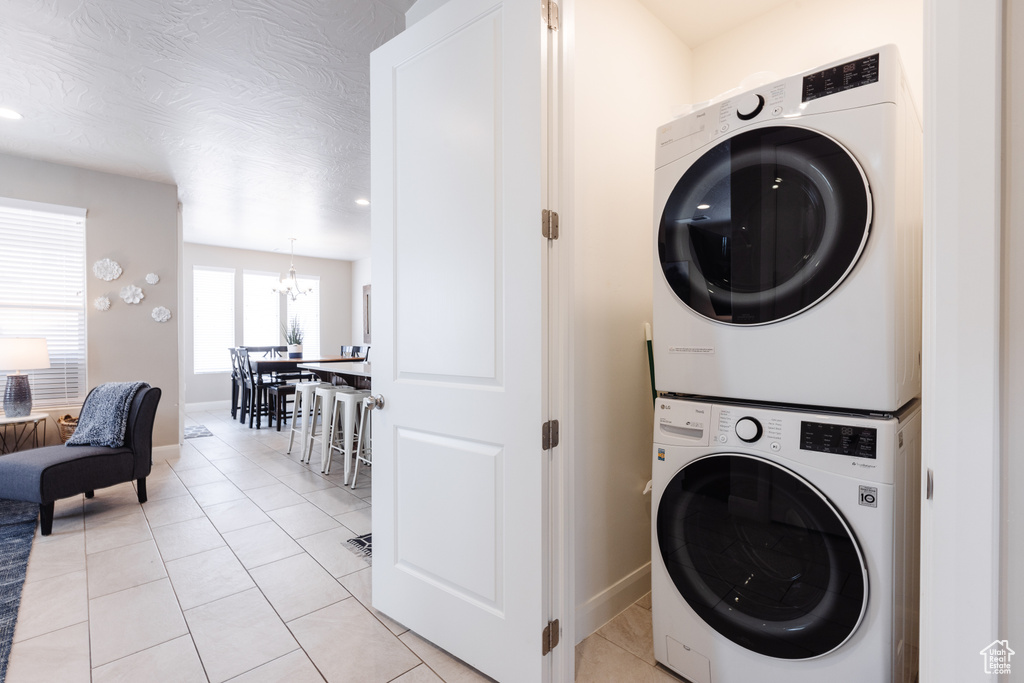 Clothes washing area with stacked washer / dryer, a chandelier, light tile patterned floors, baseboards, and recessed lighting