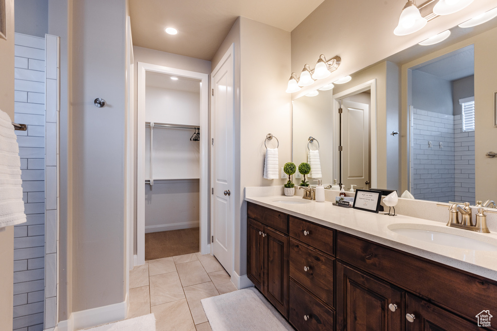 Full bathroom featuring double vanity, tile patterned flooring, a spacious closet, baseboards, and tiled shower