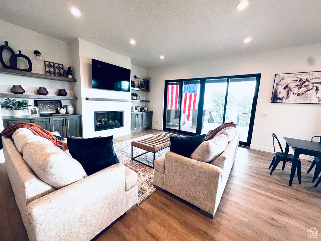 Living room with recessed lighting, light wood finished floors, a glass covered fireplace, and baseboards