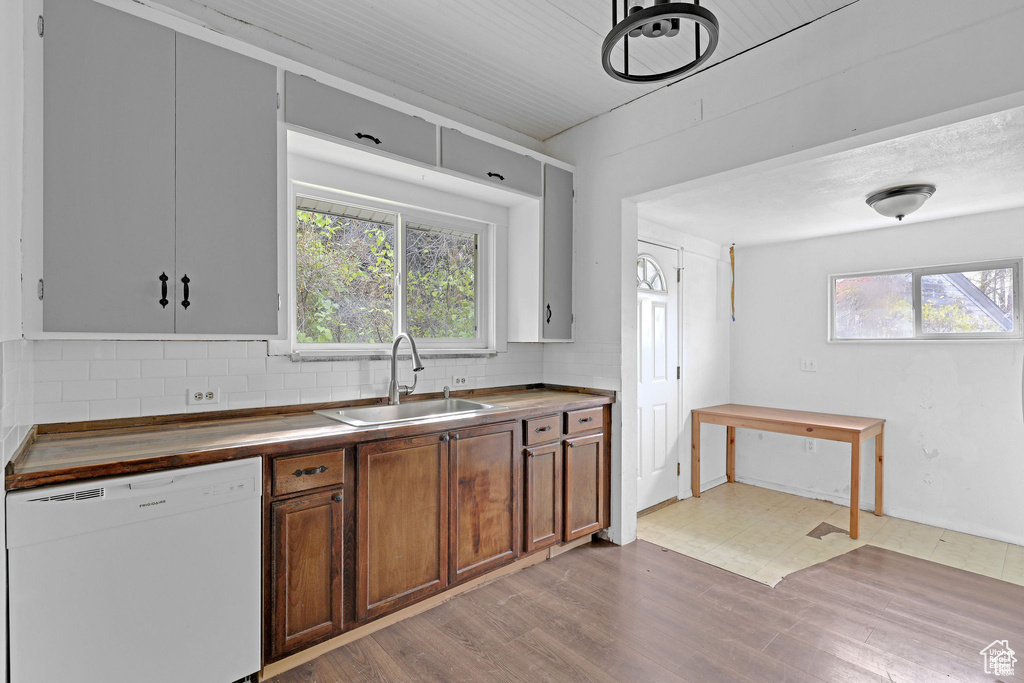 Kitchen featuring white dishwasher, a sink, tasteful backsplash, and plenty of natural light