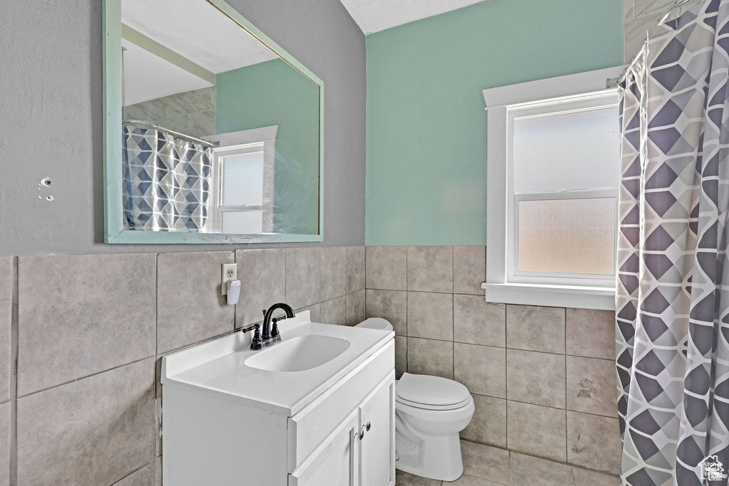 Bathroom featuring tile walls, vanity, toilet, curtained shower, and wainscoting