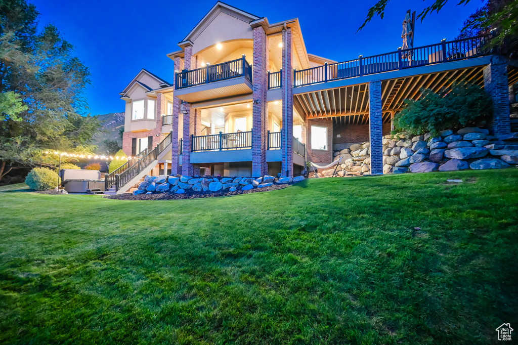 Back of house at night with stairway, a balcony, a lawn, stucco siding, and brick siding